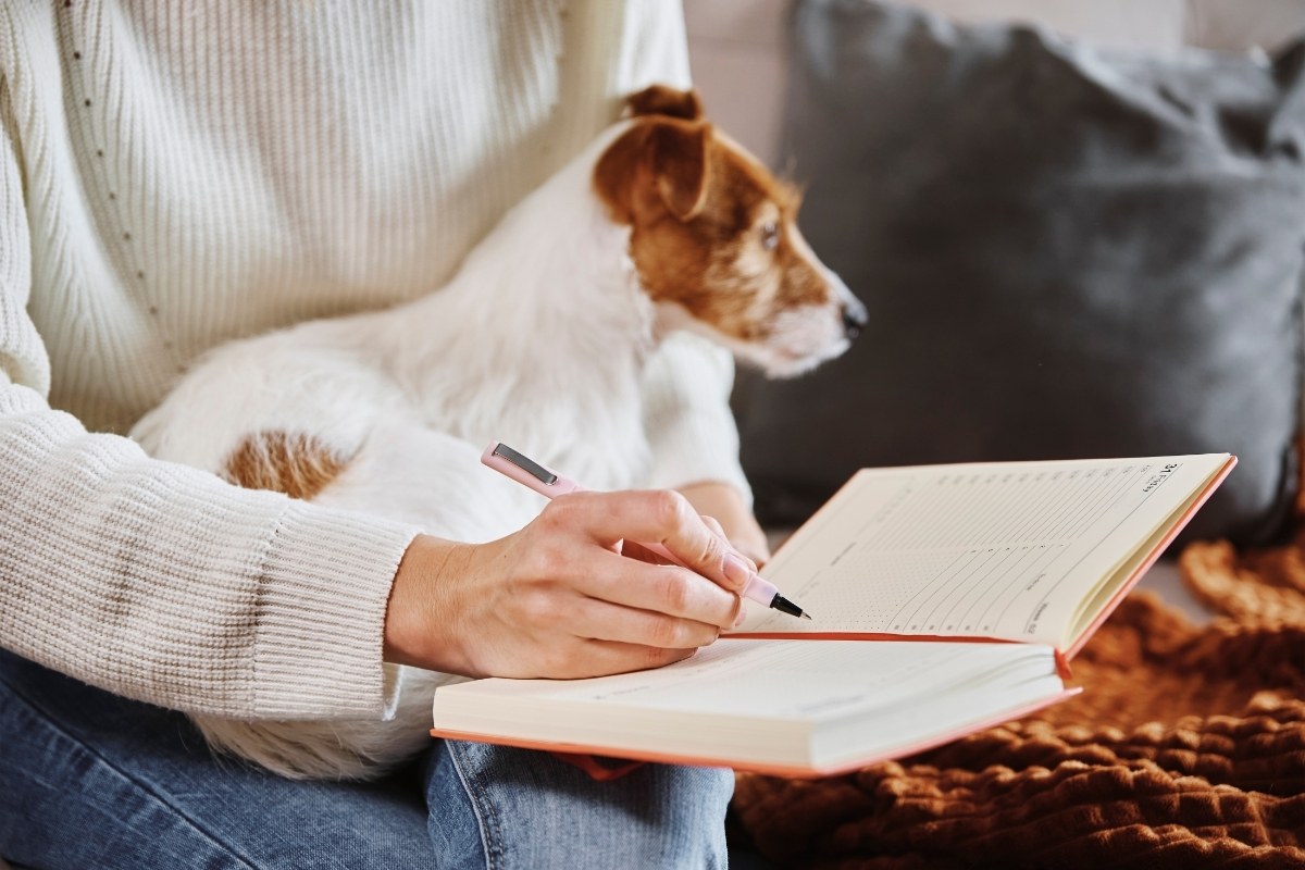 犬を膝にのせてノートに記録をつける人